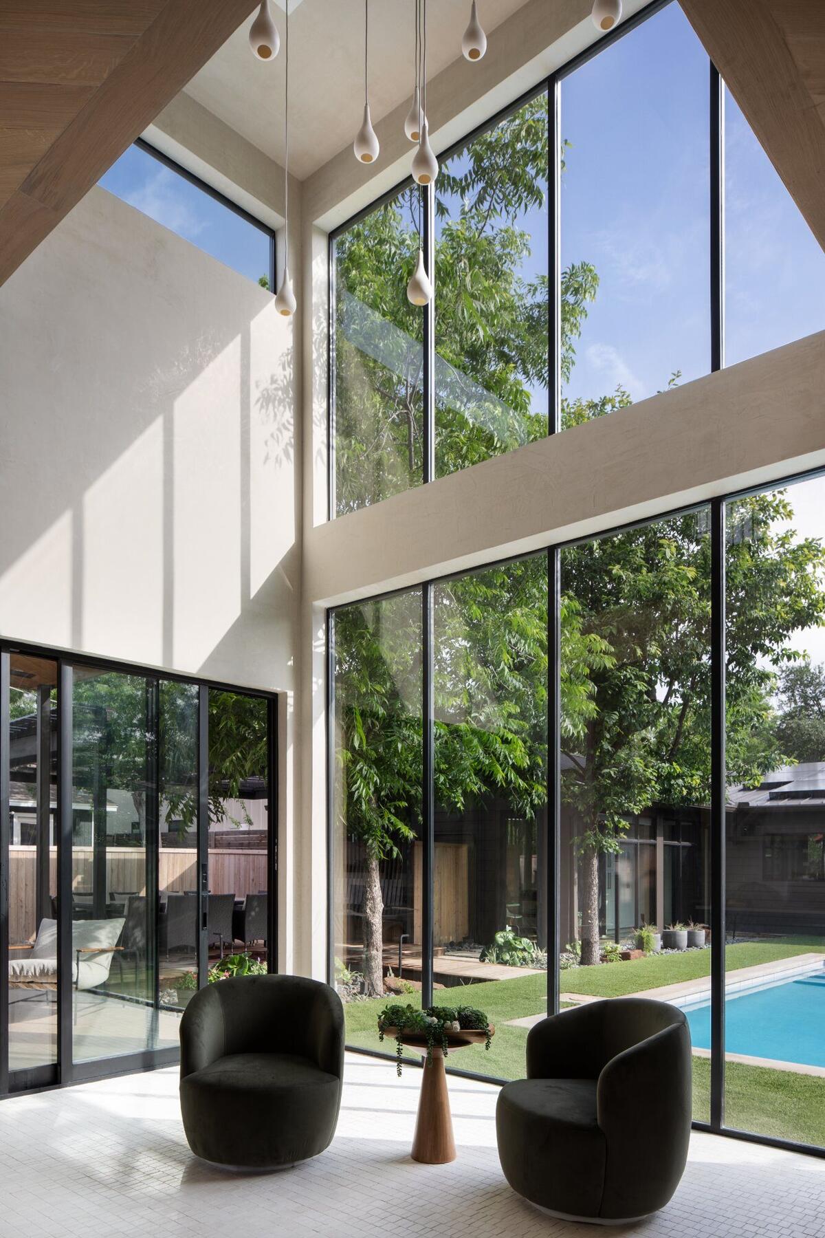 Modern living room with double-height windows overlooking pool - Lyte Custom